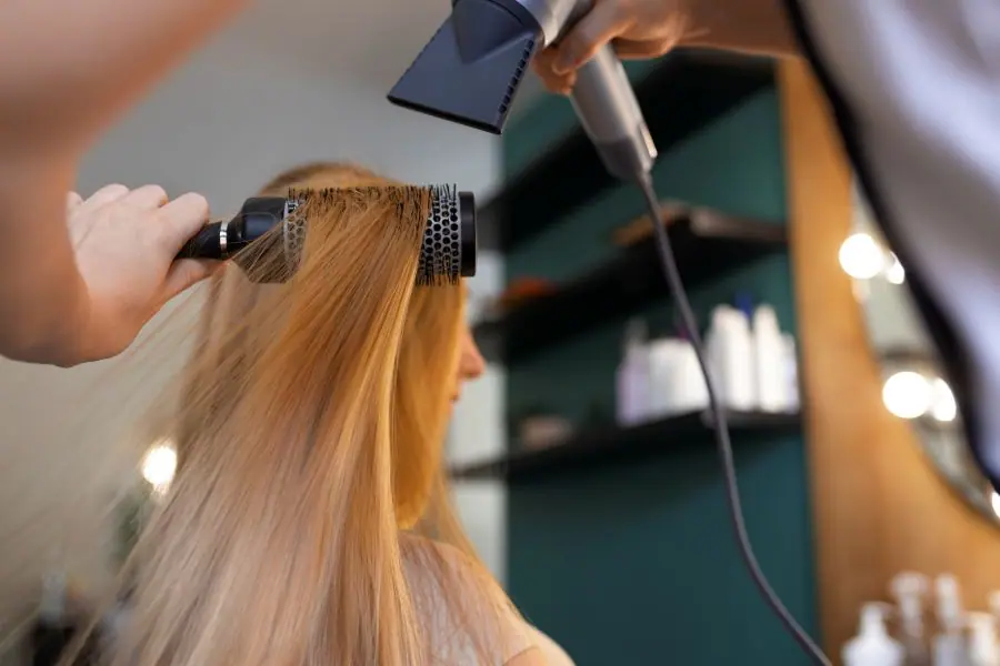 A stylist blow-drying long hair with a round brush